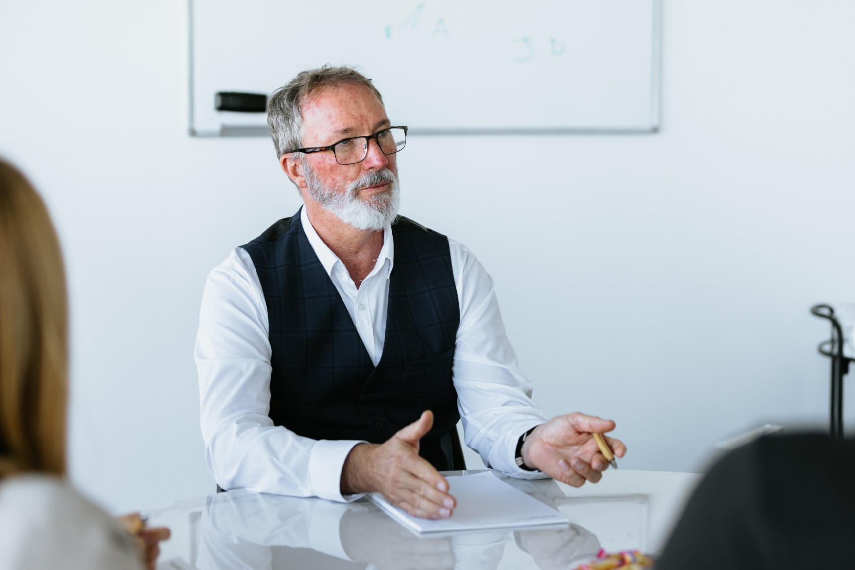 Man with grey beard and glasses explaining something to a group of lawyers